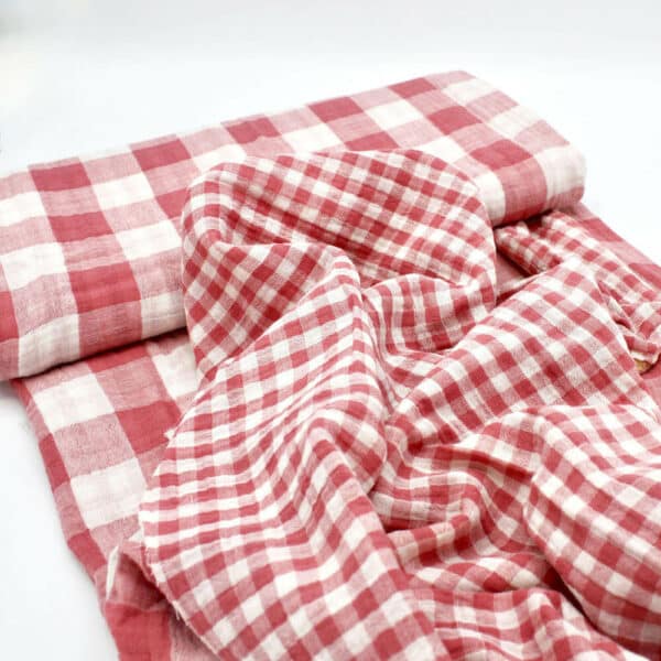 bolt of gingham double gauze cotton fabric in berry pink showing both sides of the fabric.