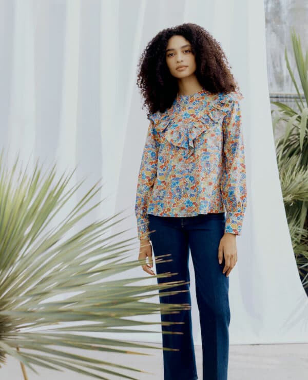 girl standing in front of some drapped fabric and a plant wearing a floral liberty print blouse