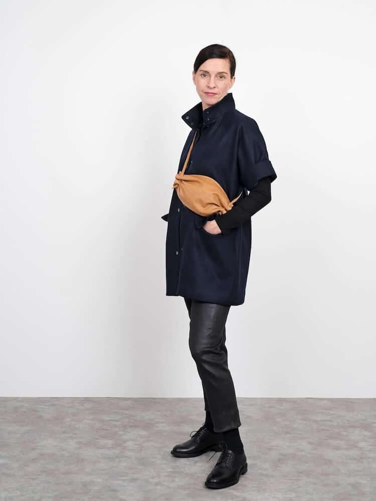 lady wearing a cap sleeve wool jacket with high collar and trousers. Also wearing a cross body tan bag.