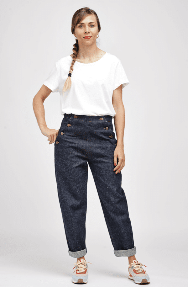 standing lady wearing a white t-shirt and denim jeans. The jeans have buttoned sailor type closures at thr hip and turn ups.
