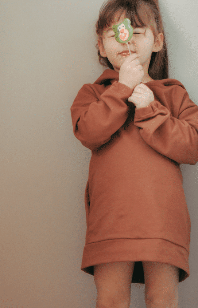 Young girl wearing a sweatshirt dress and licking a lollypip