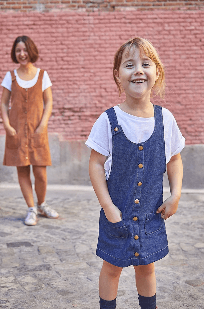 a young girl smiling wearing a blue corduroy pinafore dess