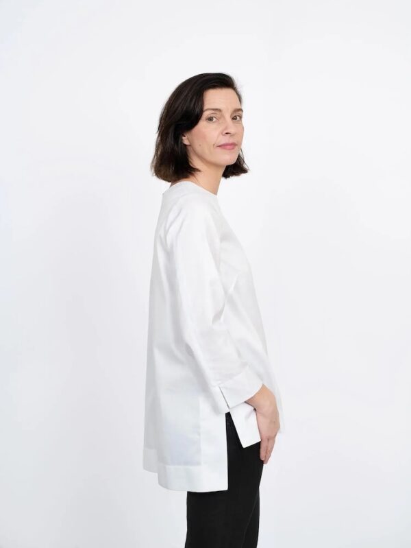 lady standing side on wearing a hip length white tunic with dipped back hem.